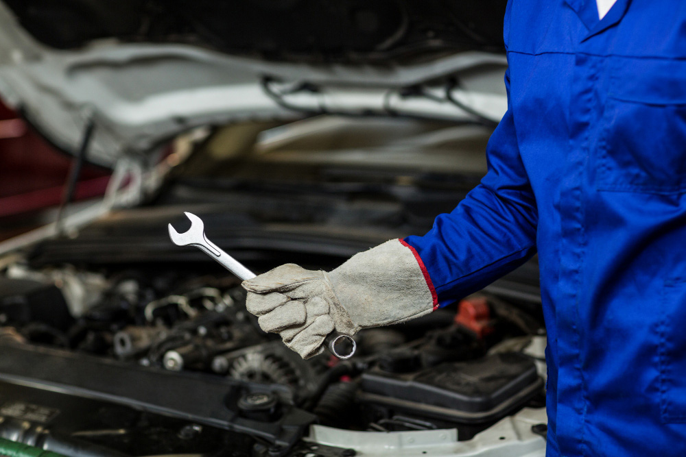 Mann hält einen Schraubenschlüssel in der Hand vor einem Auto mit einer offenen Motorhaube.
